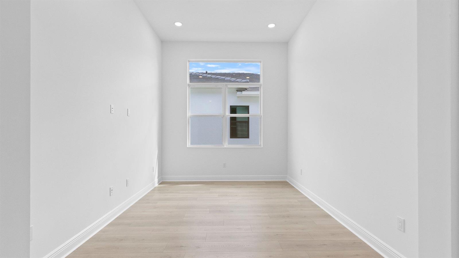 An empty room with white walls, light wood flooring, and a window facing a house — 5468 Hutchinson Way, Westlake FL 33470, WESTLAKE, FL