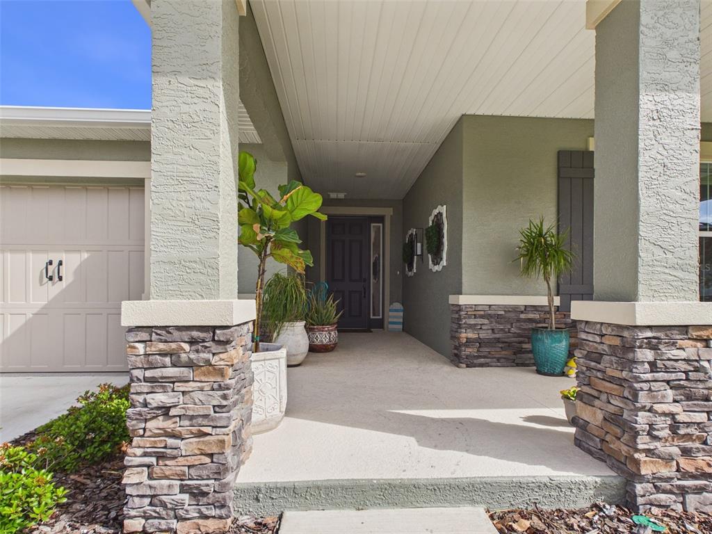 A covered front porch features stone-accented columns, potted plants, and a dark front door — 7545 SW 56TH PLACE, OCALA, FL