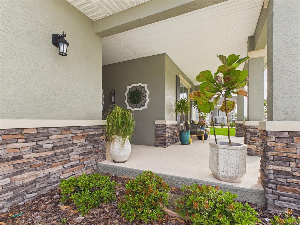 A covered front porch features stone veneer siding, potted plants, and a concrete floor — 7545 SW 56TH PLACE, OCALA, FL