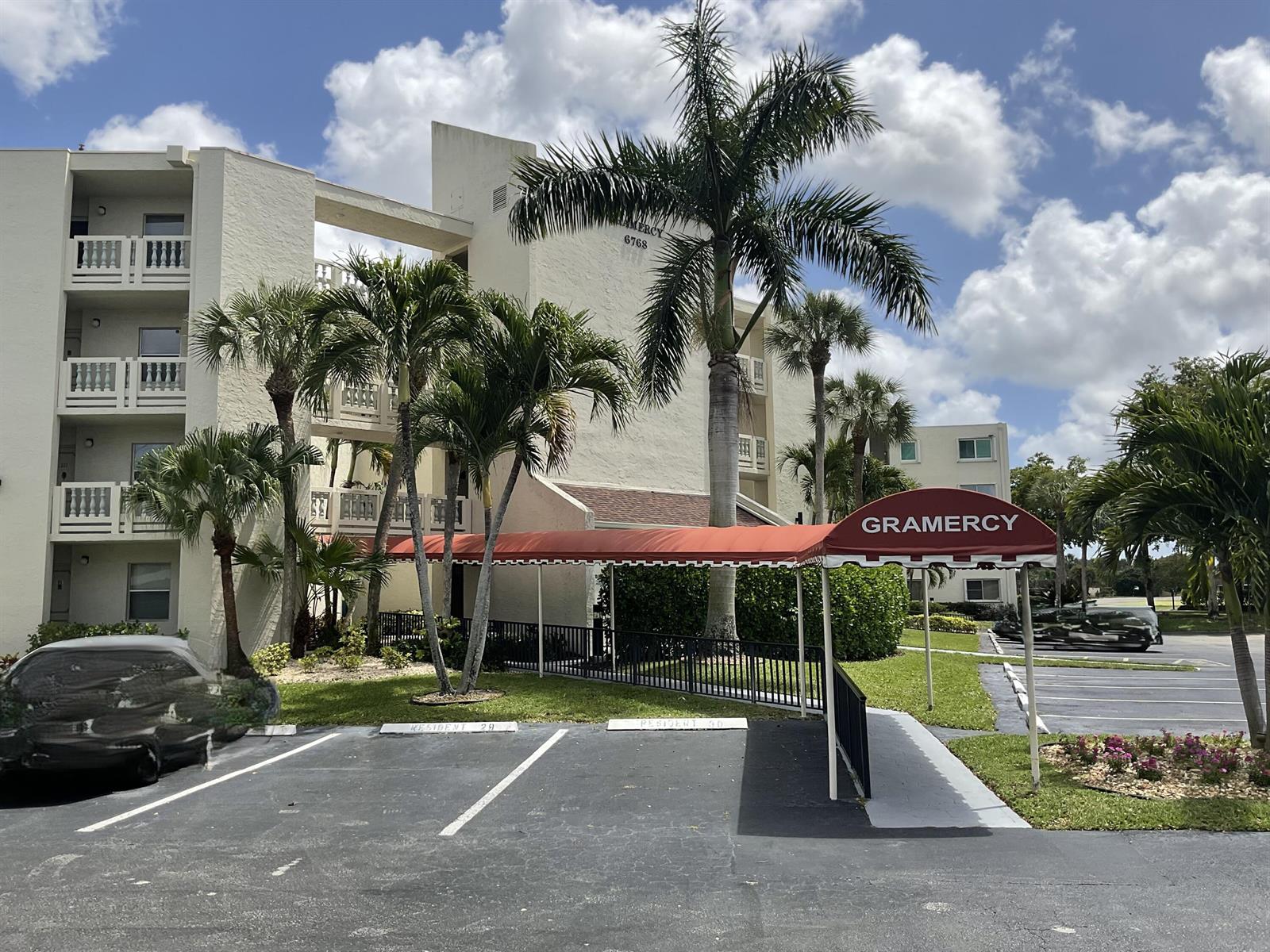 An exterior view of a multi-story apartment building with a red awning and palm trees — 6768 N 10th Ave N # 209, Lake Worth FL 33467, LAKE WORTH, FL