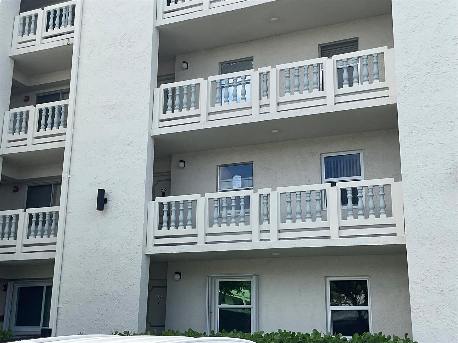 The exterior of a multi-story apartment building features white stucco walls and white balcony railings — 6768 N 10th Ave N # 209, Lake Worth FL 33467, LAKE WORTH, FL