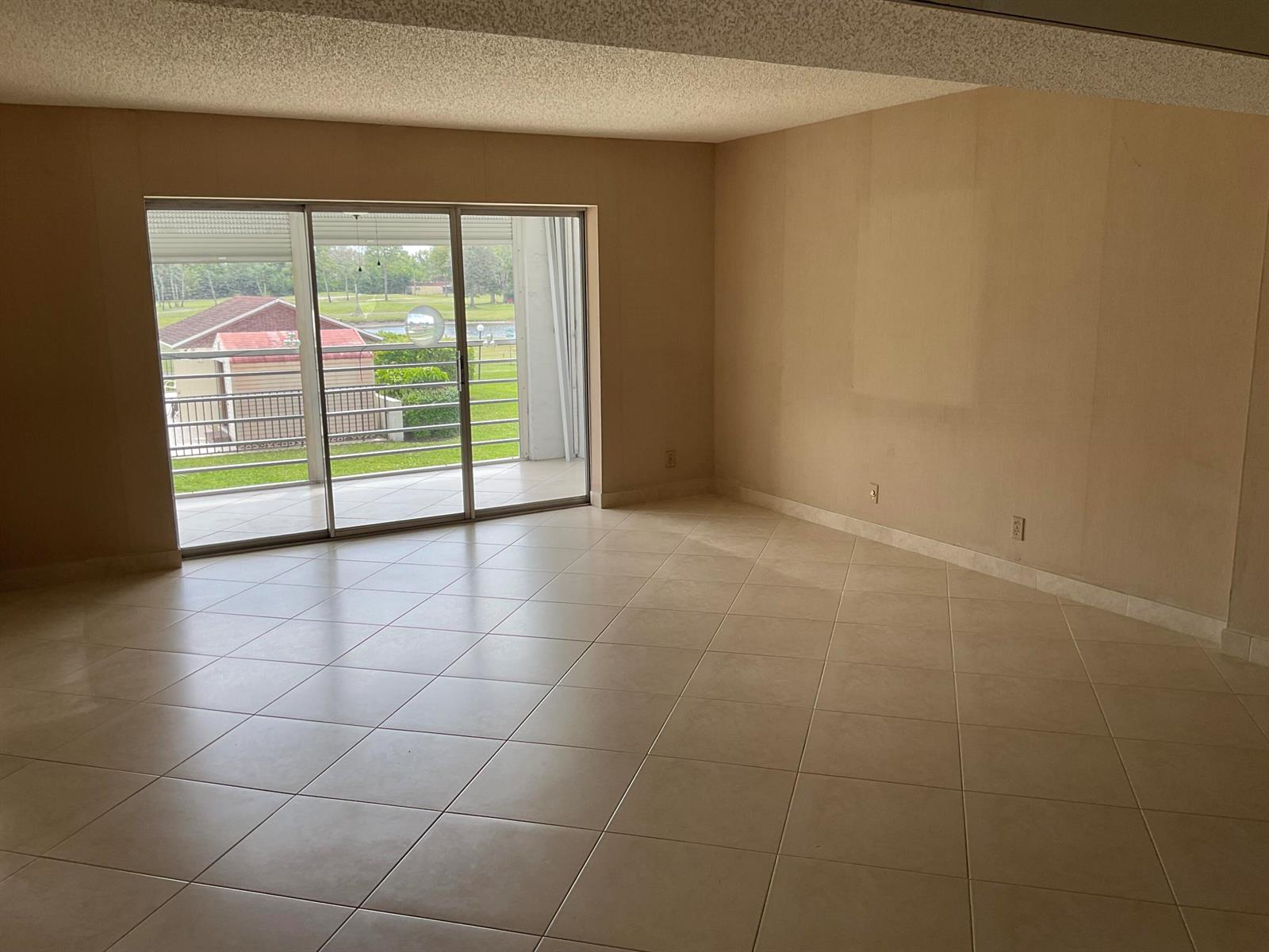 An empty living room with beige tile floors, tan walls, and a sliding glass door — 6768 N 10th Ave N # 209, Lake Worth FL 33467, LAKE WORTH, FL