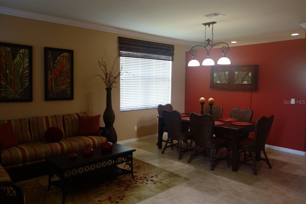 A dining and living area features a red accent wall, wicker chairs, and tile flooring — 339 RIVER ENCLAVE COURT, BRADENTON, FL