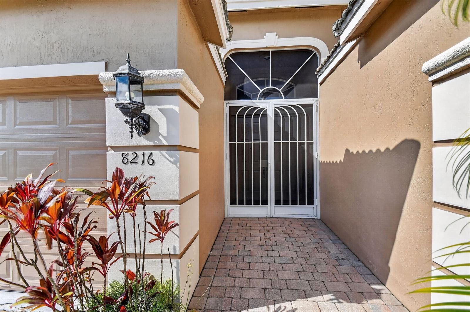 A paved walkway leads to a white metal screen door at the home's entrance — 8216 Parini Way, Lake Worth FL 33467, LAKE WORTH, FL