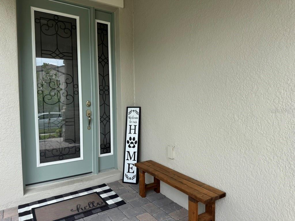 A front entryway features a light green door, a wooden bench, and a welcome sign — 7749 BRONZE OAK DRIVE, WESLEY CHAPEL, FL