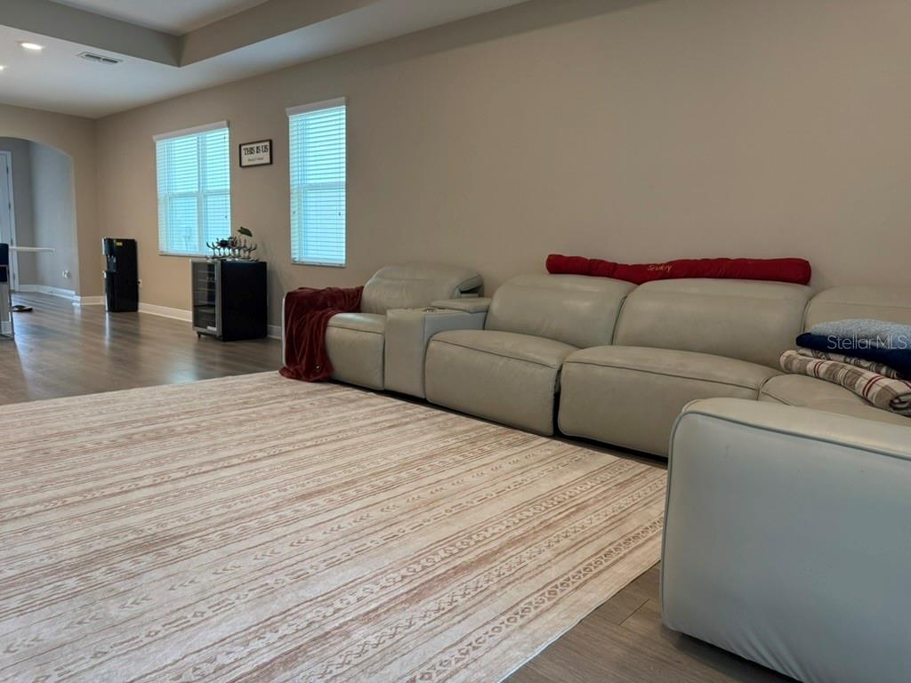 A living room features a large light-colored sectional sofa, a patterned area rug, and windows — 7749 BRONZE OAK DRIVE, WESLEY CHAPEL, FL
