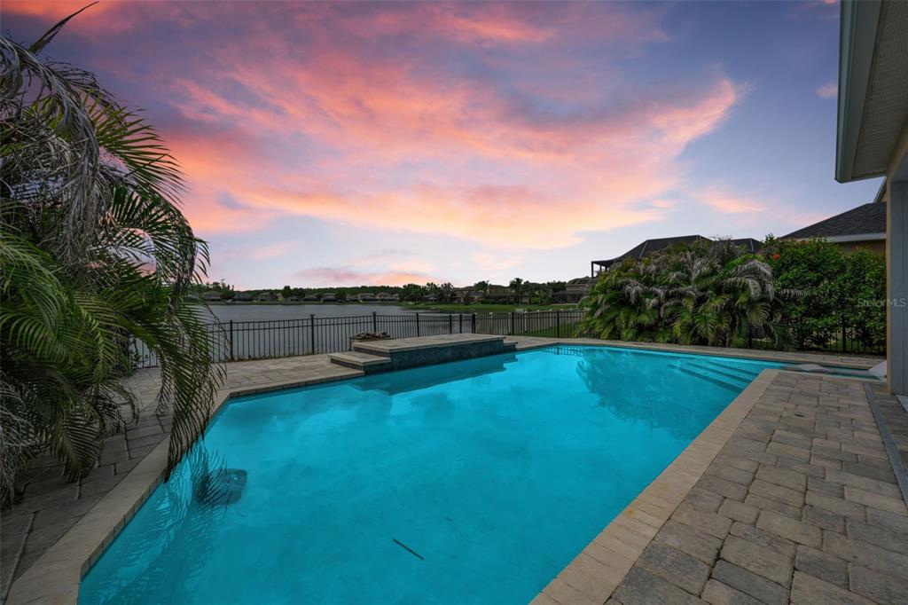 A swimming pool with a raised spa overlooks a lake at sunset — 1345 HALAPA WAY, TRINITY, FL