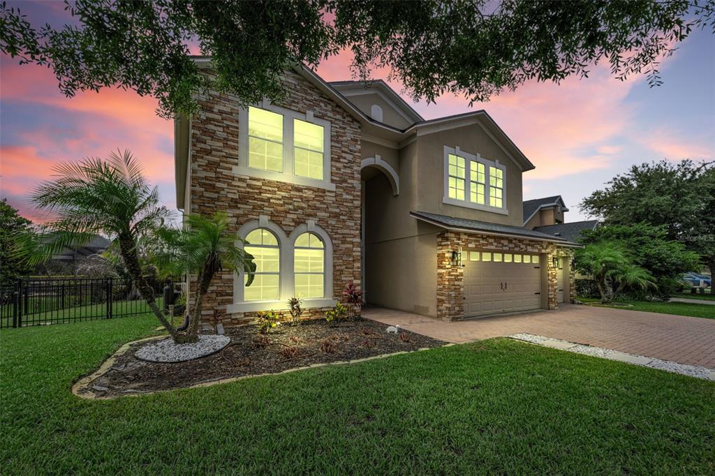 A two-story house with stone veneer, a paved driveway, and a garage at sunset — 1345 HALAPA WAY, TRINITY, FL