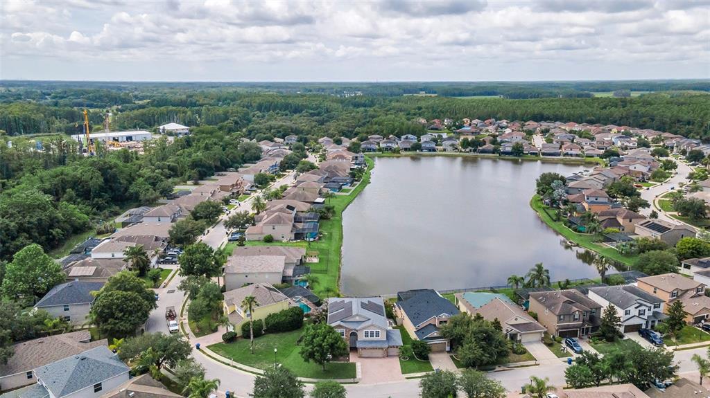 An aerial view shows a suburban neighborhood with houses surrounding a central lake — 1345 HALAPA WAY, TRINITY, FL
