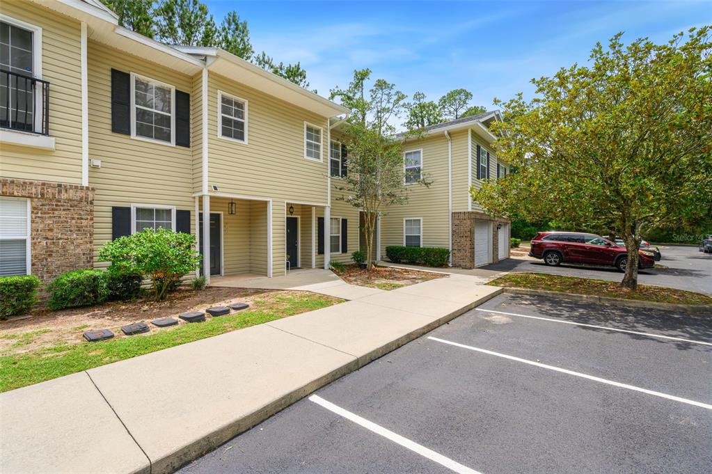 A two-story tan townhouse with a concrete walkway and a parking lot in front — 5065 NW 45TH ROAD UNIT 102, GAINESVILLE, FL