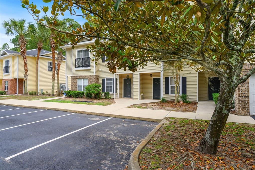A two-story apartment building with yellow siding, a paved parking lot, and a large tree — 5065 NW 45TH ROAD UNIT 102, GAINESVILLE, FL