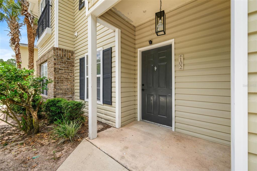 The exterior entrance of a building features a dark gray door and light siding — 5065 NW 45TH ROAD UNIT 102, GAINESVILLE, FL