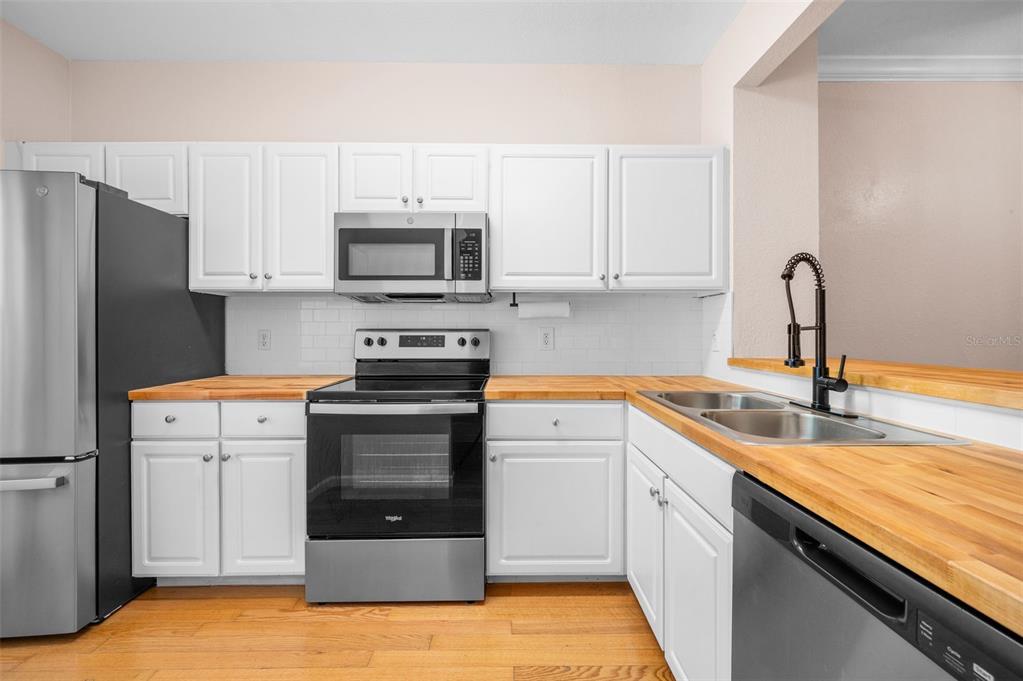 A kitchen features white cabinets, butcher block countertops, stainless steel appliances, and hardwood flooring — 5065 NW 45TH ROAD UNIT 102, GAINESVILLE, FL