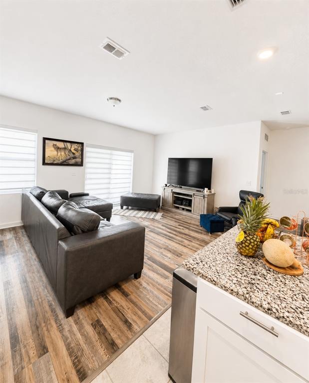 A living room with wood-look flooring, a dark leather sectional, and a television on a console — 5882 HERDER ROAD, ST CLOUD, FL