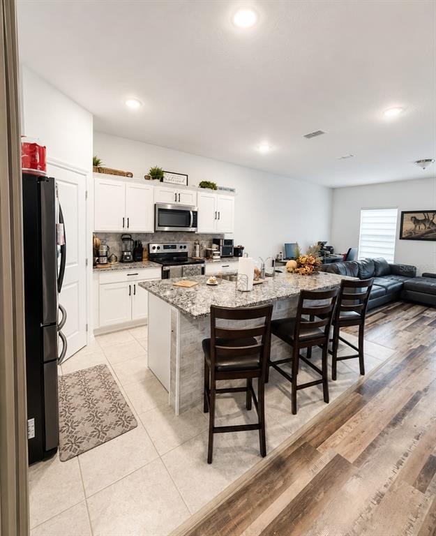 A kitchen features white cabinets, granite countertops, a center island with bar seating, and tile flooring — 5882 HERDER ROAD, ST CLOUD, FL