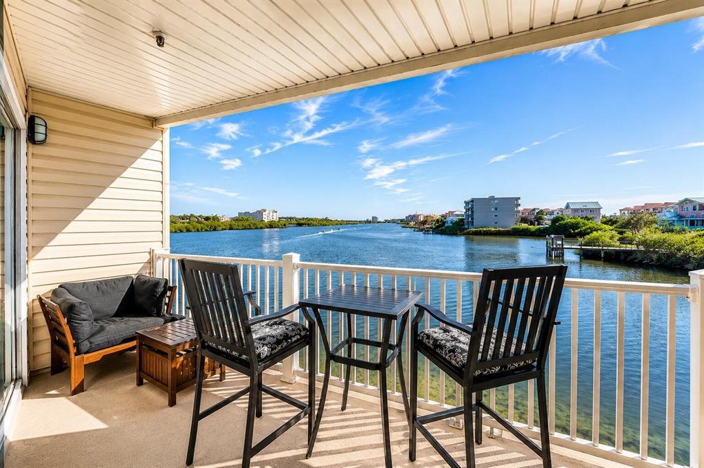 A balcony with outdoor furniture overlooks a river with buildings and vegetation in the distance — 19811 GULF BOULEVARD UNIT 102, INDIAN SHORES, FL