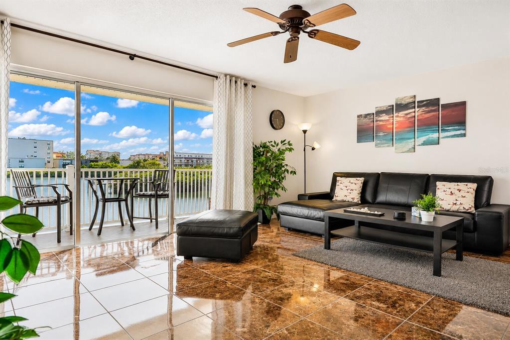 A living room with brown tile floors, a black leather sofa, and a balcony overlooking water — 19811 GULF BOULEVARD UNIT 102, INDIAN SHORES, FL