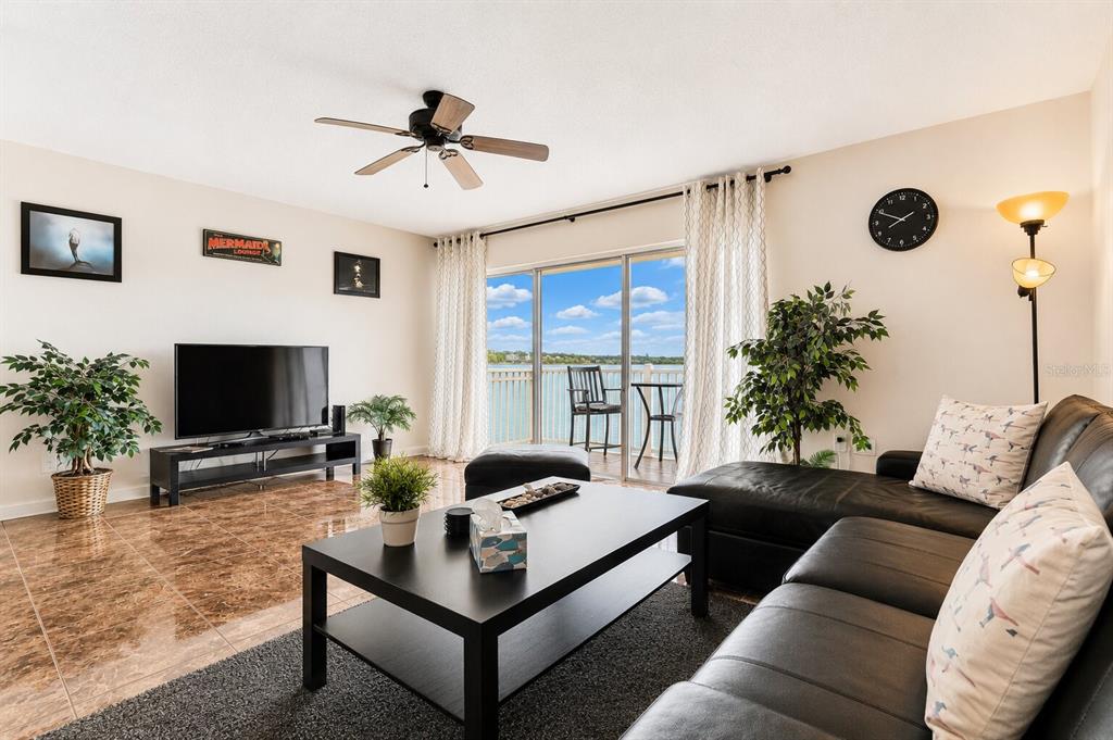 A living room features tile flooring, a black leather sectional, and a balcony with water views — 19811 GULF BOULEVARD UNIT 102, INDIAN SHORES, FL
