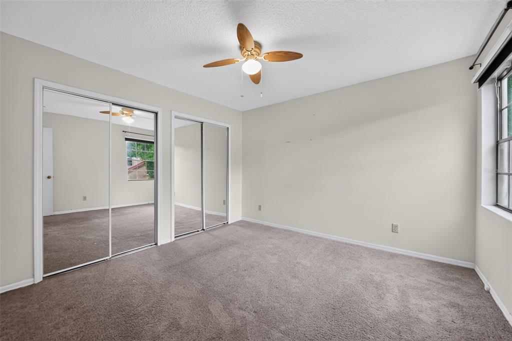 A bedroom with beige walls, gray carpeting, mirrored closet doors, and a ceiling fan — 1375 AUGUSTA NATIONAL BOULEVARD, WINTER SPRINGS, FL