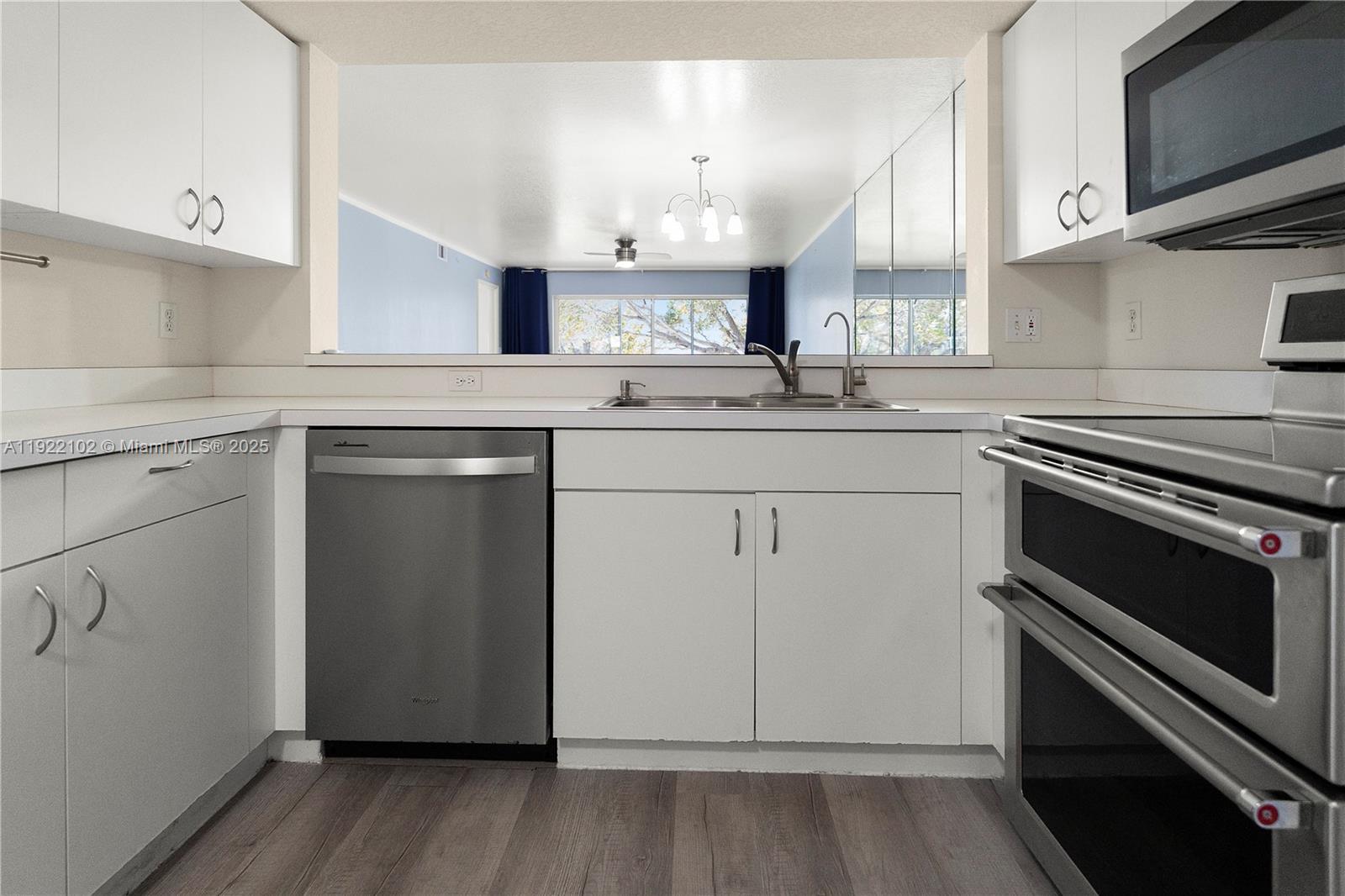 A kitchen features white cabinets, stainless steel appliances, and a pass-through window to the living area — 9610 VICTORIA LANE # D202, Naples FL 34109, NAPLES, FL