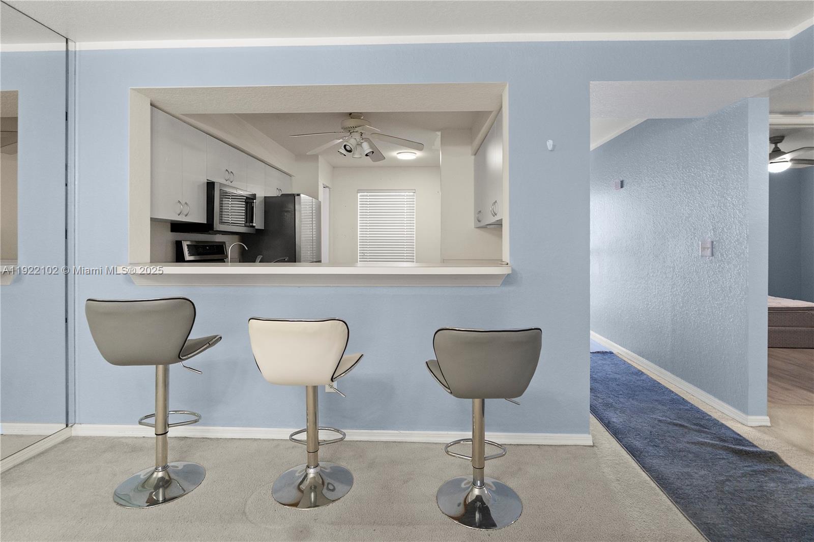 A kitchen pass-through window overlooks a breakfast bar with three stools in a room — 9610 VICTORIA LANE # D202, Naples FL 34109, NAPLES, FL