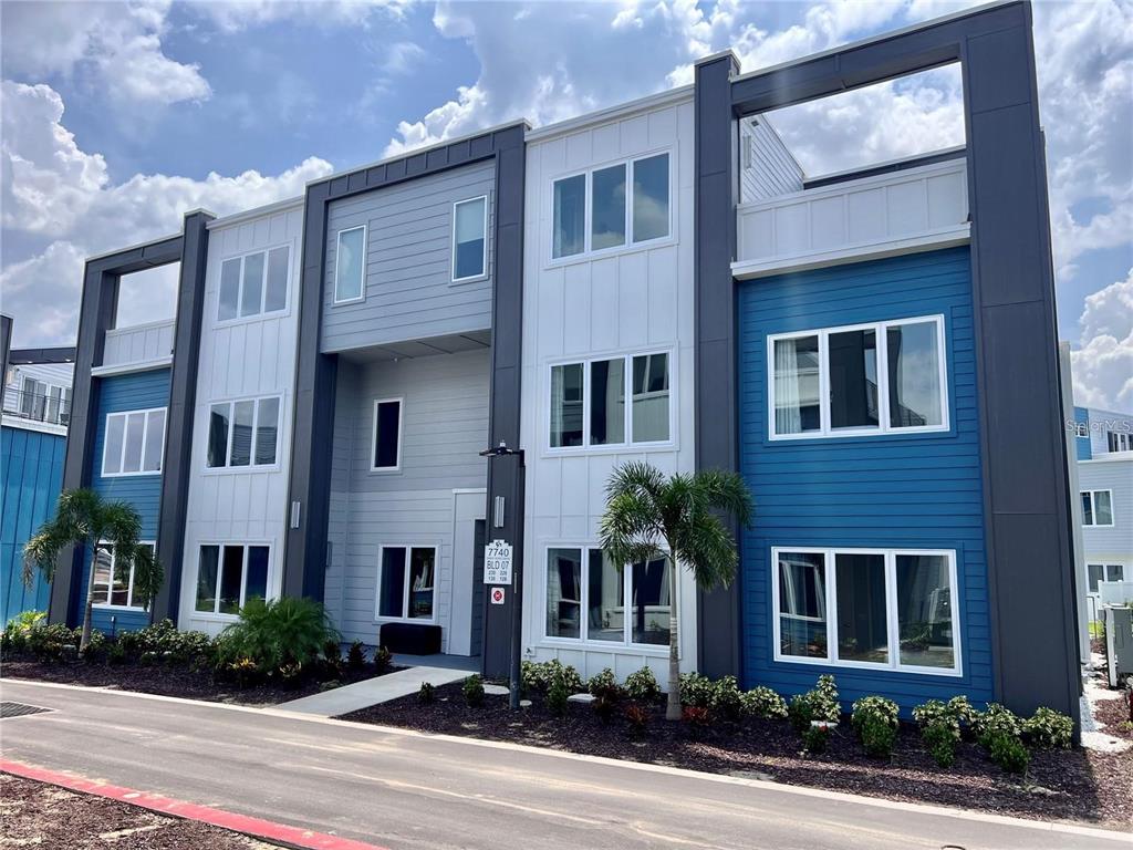 A three-story apartment building features blue, grey, and white siding with large rectangular windows — 7740 SANDY RIDGE DRIVE UNIT 228, KISSIMMEE, FL