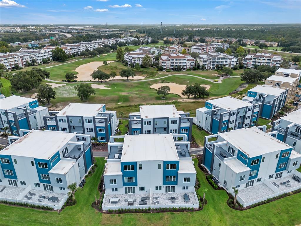 An aerial view shows modern multi-story residential buildings situated next to a golf course — 7740 SANDY RIDGE DRIVE UNIT 228, KISSIMMEE, FL