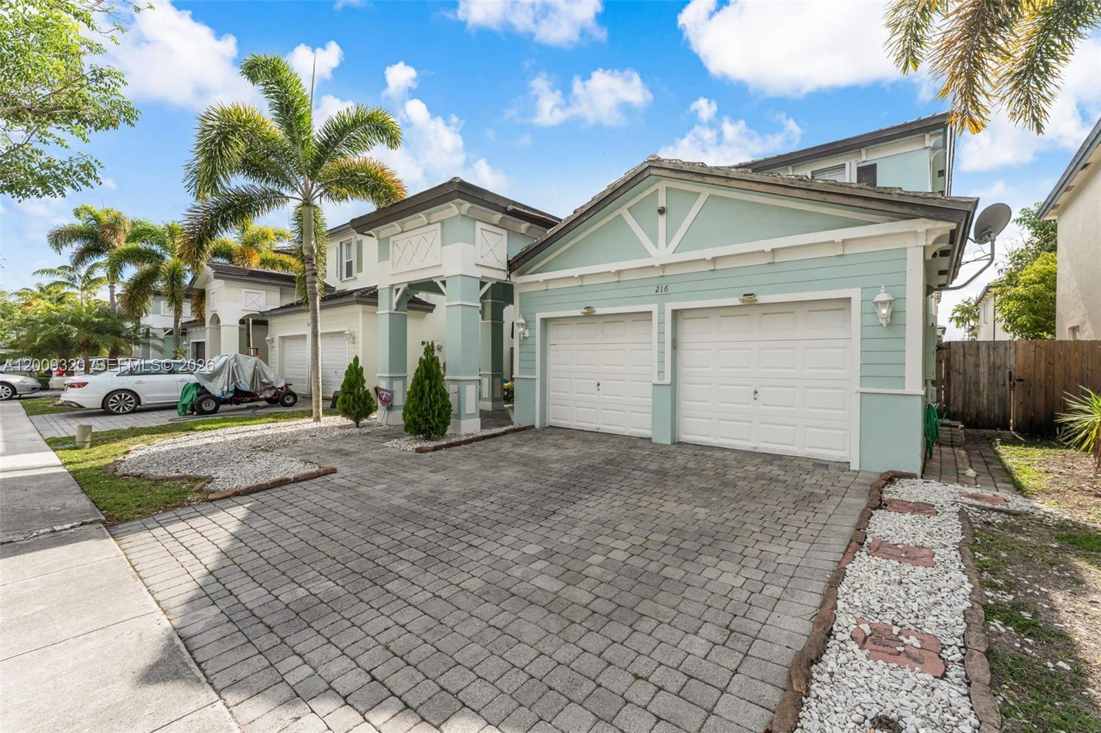 A two-story, light green house features a two-car garage and a paved driveway — 216 NE 36th Ter, Homestead FL 33033, HOMESTEAD, FL
