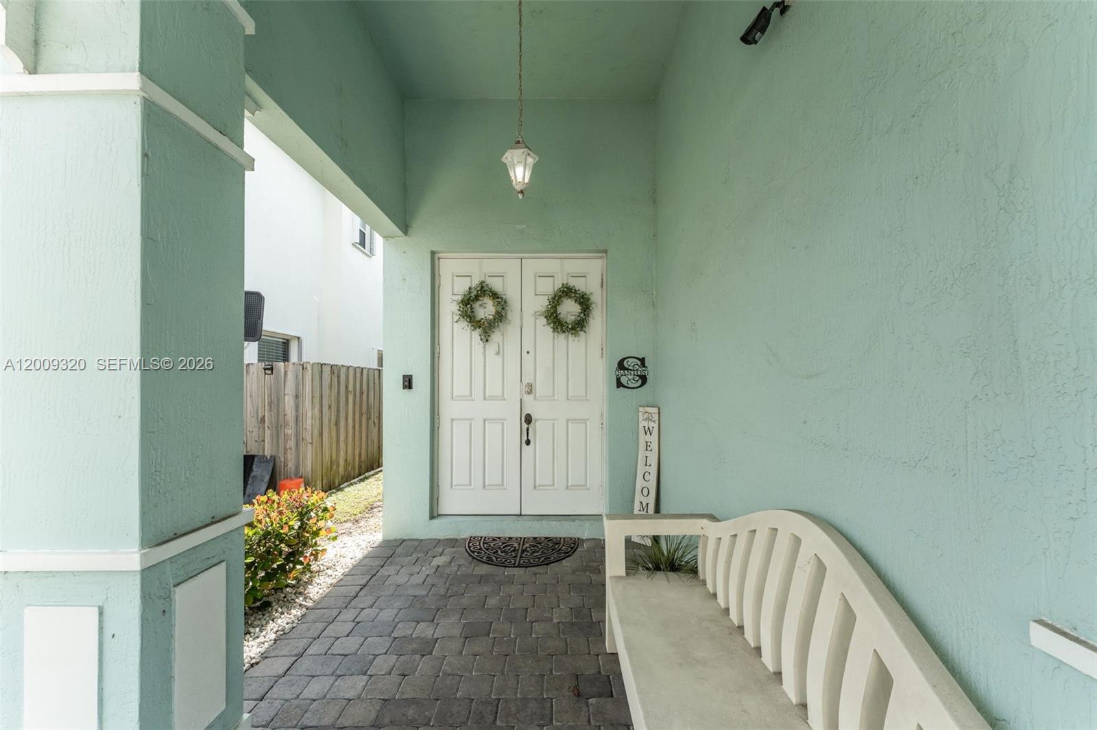 A covered front porch features a light green wall, white double doors, and a stone patio — 216 NE 36th Ter, Homestead FL 33033, HOMESTEAD, FL