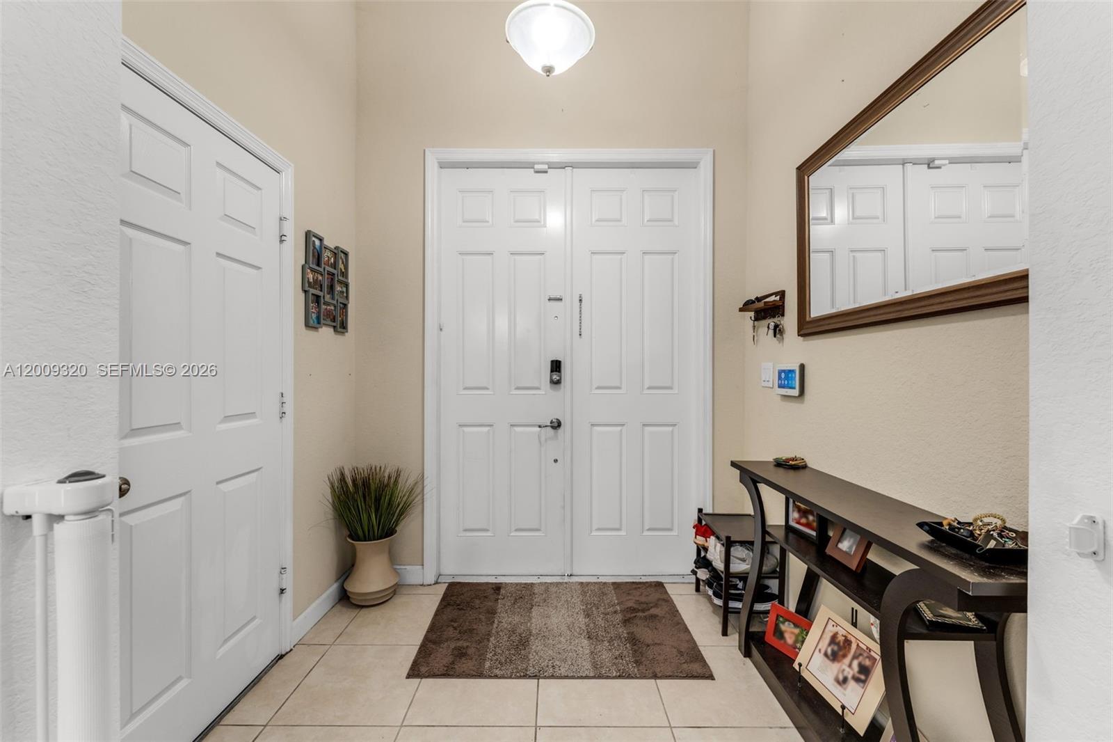 This entryway features a double front door, tile flooring, a console table, and a mirror — 216 NE 36th Ter, Homestead FL 33033, HOMESTEAD, FL