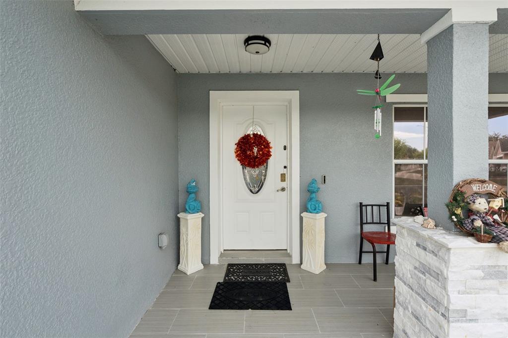 A covered front porch features a white door with a wreath, tile flooring, and decor — 7506 FORDHAM CREEK LANE, ORLANDO, FL