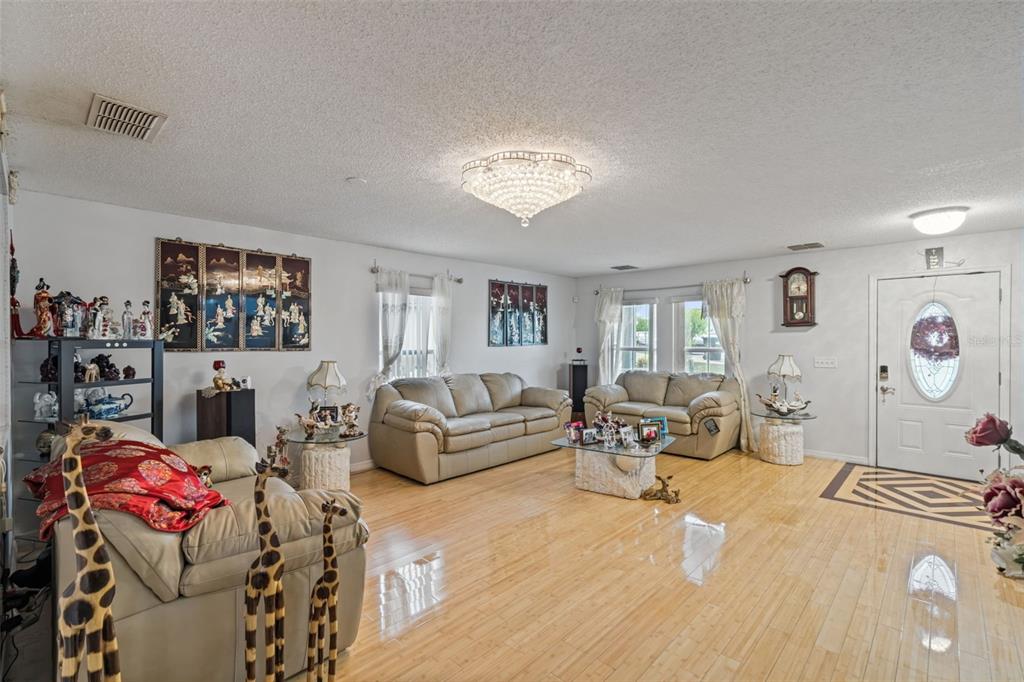 A living room features light wood flooring, beige leather sofas, and a crystal ceiling fixture — 7506 FORDHAM CREEK LANE, ORLANDO, FL