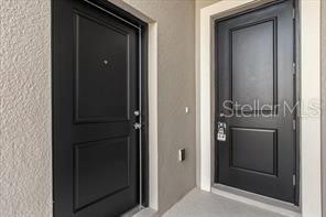 Two black doors with rectangular panels are set into a light-colored exterior wall — 4385 PEBBLES THROW DRIVE UNIT B, KISSIMMEE, FL