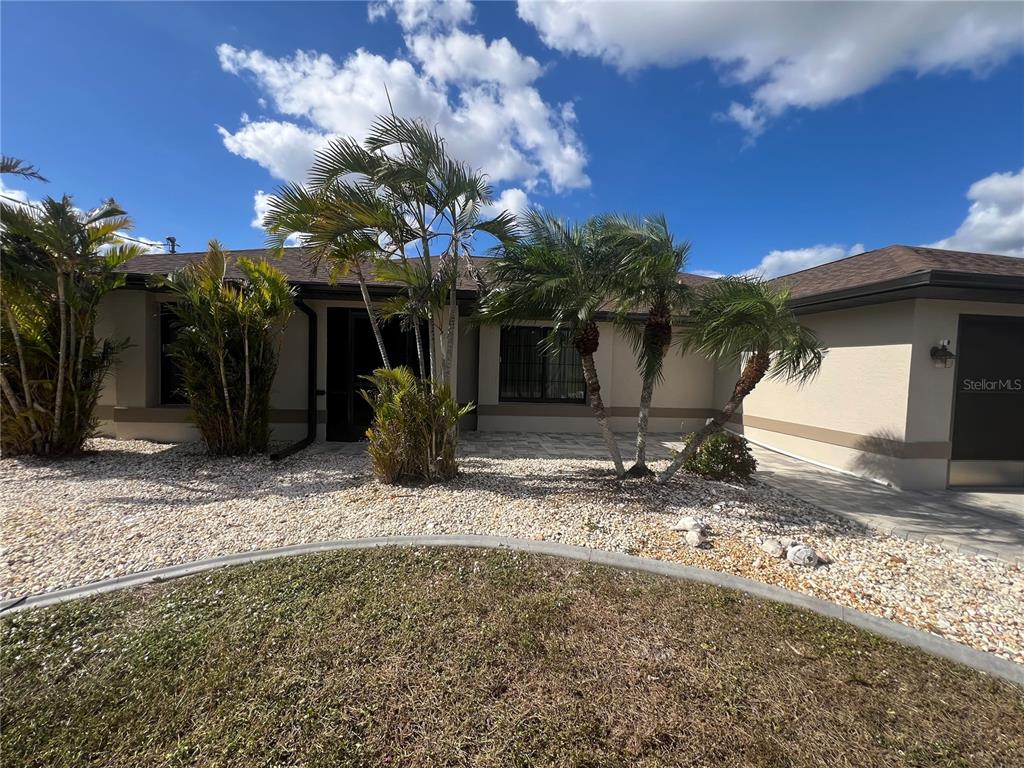 A one-story house exterior features a stone-covered yard, palm trees, and a paved walkway — 3177 CLIFFORD STREET, PUNTA GORDA, FL