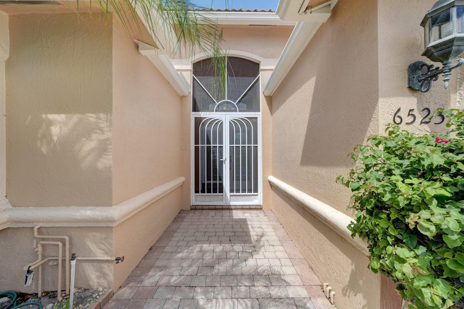 A paved walkway leads to a white metal screen door at the home's entrance — 6523 Via Trento, Delray Beach FL 33446, DELRAY BEACH, FL