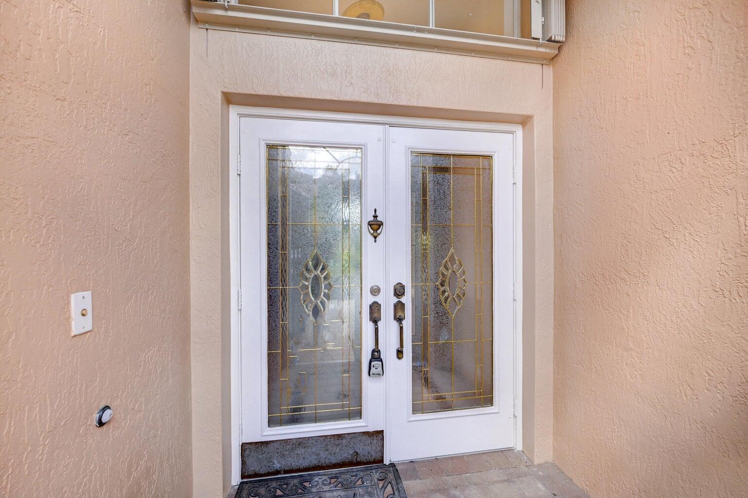 A set of white double doors with decorative glass panels sits in a stucco entryway — 6523 Via Trento, Delray Beach FL 33446, DELRAY BEACH, FL