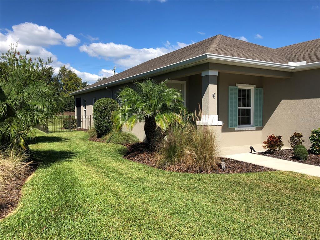 A tan house exterior features a covered entryway, palm trees, and a manicured lawn — 13544 OLD CREEK COURT, PARRISH, FL