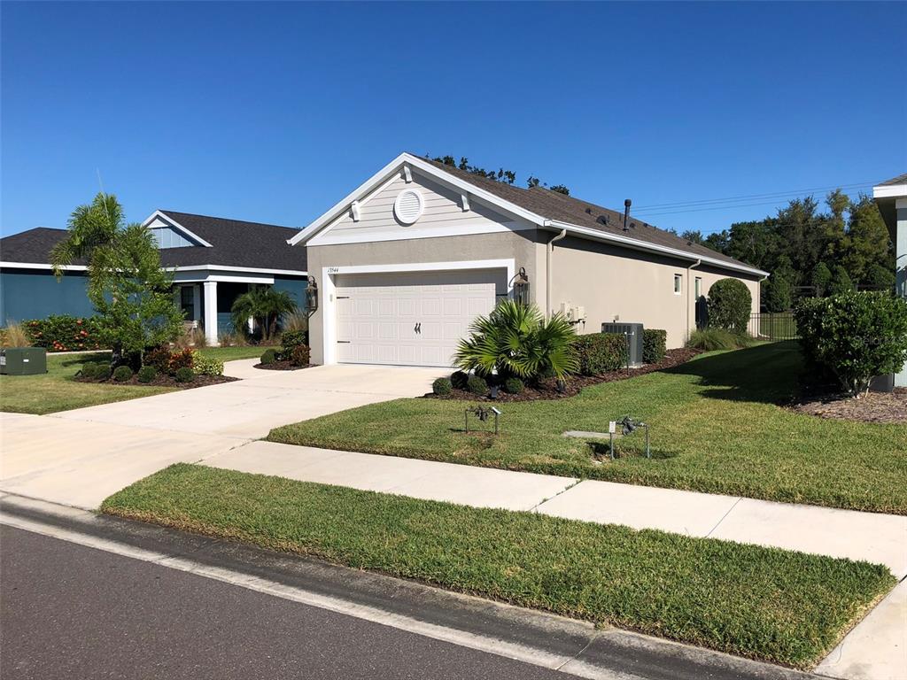 A beige single-story house with a two-car garage and a landscaped front yard — 13544 OLD CREEK COURT, PARRISH, FL