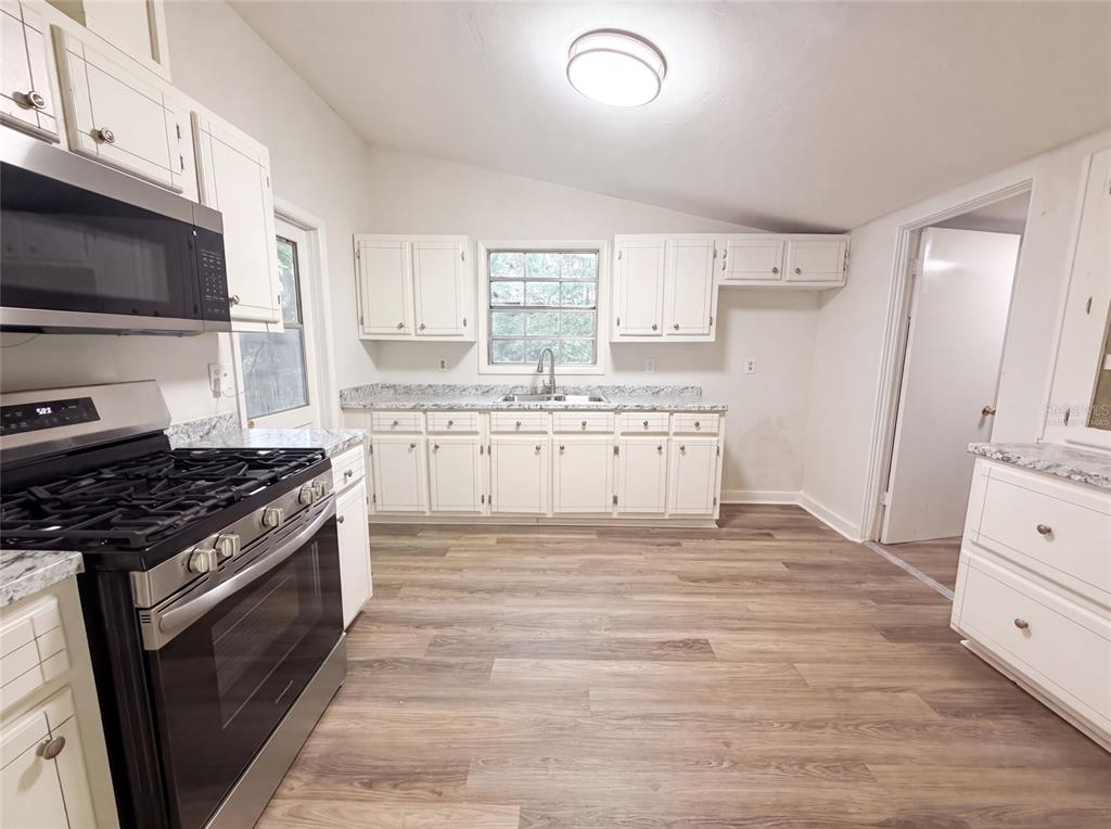 A kitchen features white cabinets, stainless steel appliances, granite countertops, and wood-look flooring — 1034 NE 31ST AVENUE, GAINESVILLE, FL