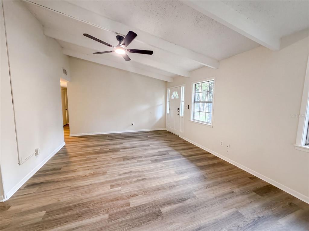 An empty living room features vaulted ceilings with exposed beams, wood-look flooring, and a ceiling fan — 1034 NE 31ST AVENUE, GAINESVILLE, FL