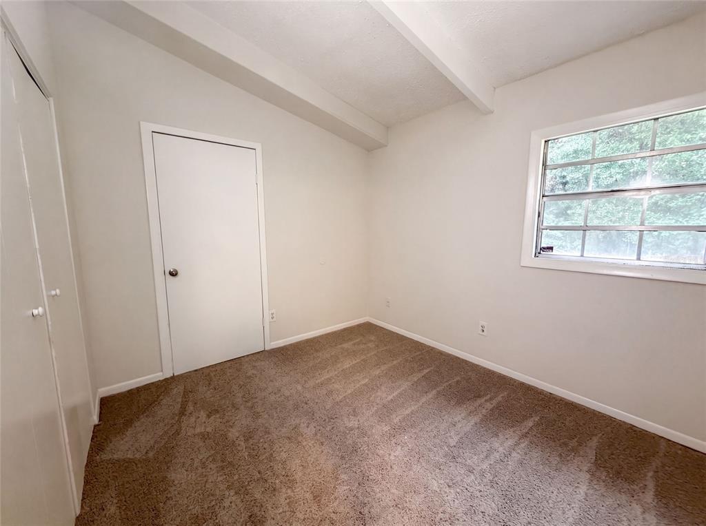A small bedroom features beige carpet, white walls, a closet, and a single window — 1034 NE 31ST AVENUE, GAINESVILLE, FL