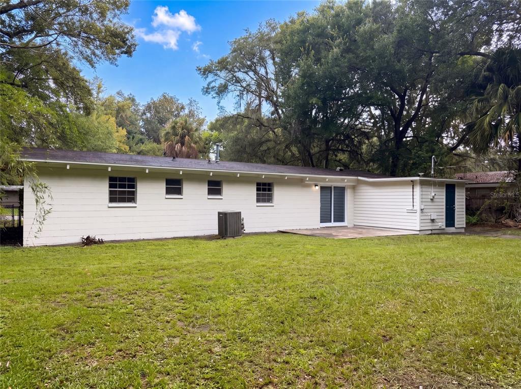 The exterior rear view of a single-story house features white siding, a patio, and trees — 1034 NE 31ST AVENUE, GAINESVILLE, FL