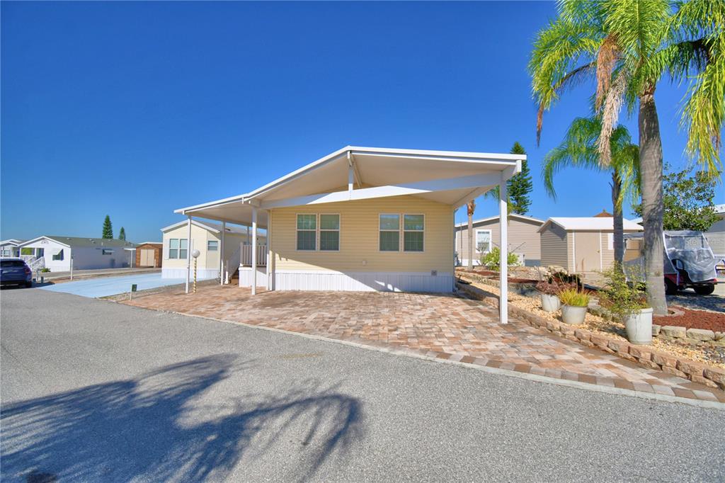 A yellow manufactured home features a paved driveway, a carport, and a palm tree — 251 PATTERSON ROAD UNIT i46, HAINES CITY, FL