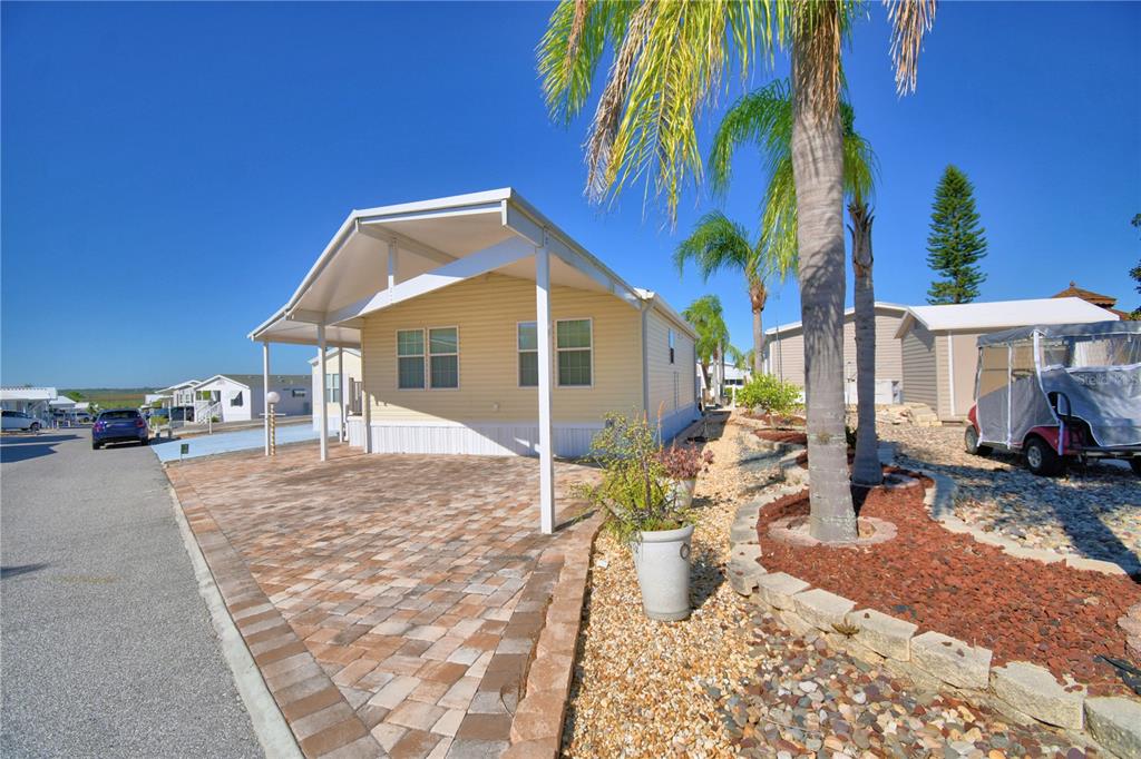 A light yellow mobile home features a paved driveway and a covered carport area — 251 PATTERSON ROAD UNIT i46, HAINES CITY, FL
