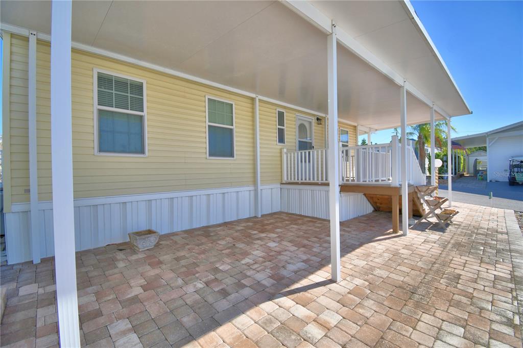 A paved patio sits beneath a covered carport next to a yellow mobile home — 251 PATTERSON ROAD UNIT i46, HAINES CITY, FL