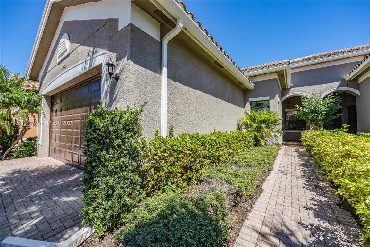 A paved walkway leads to the entrance of a house with a brown garage door — 13458 Sumter Lane, Naples FL 34109, NAPLES, FL