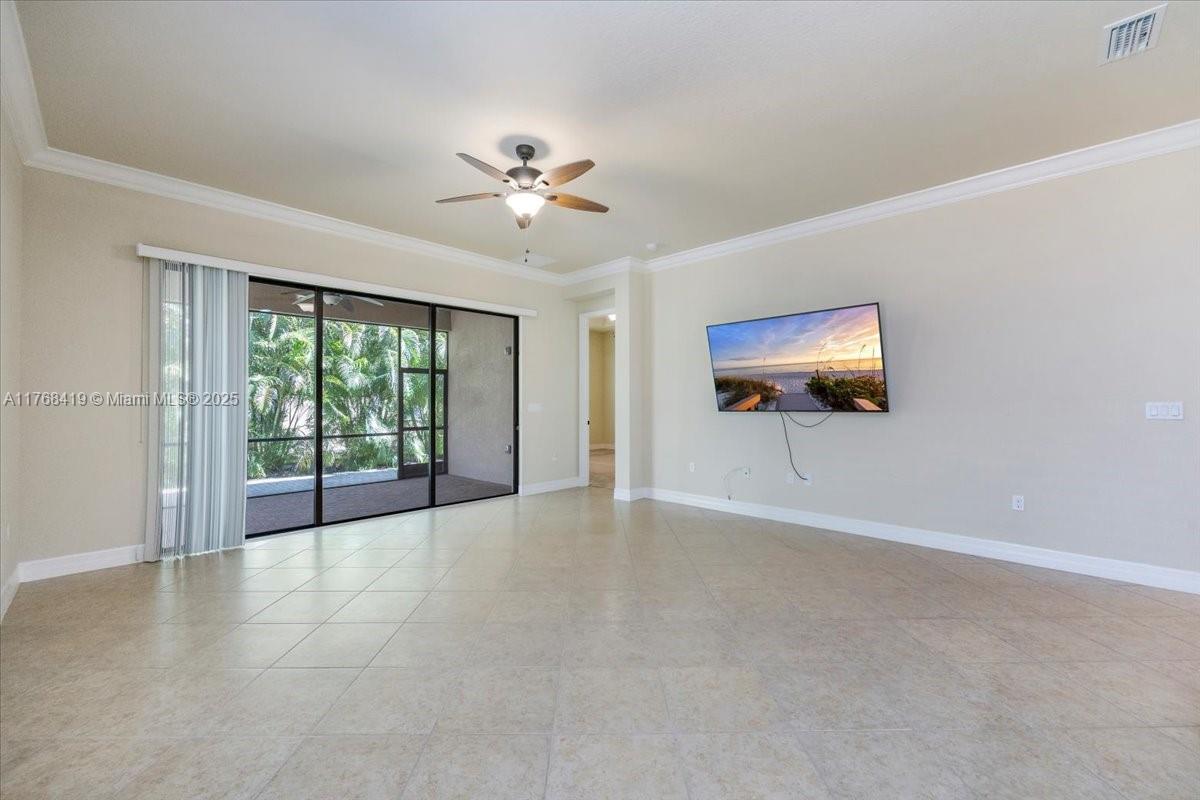 A living room features beige tile flooring, a ceiling fan, and a wall-mounted television — 13458 Sumter Lane, Naples FL 34109, NAPLES, FL