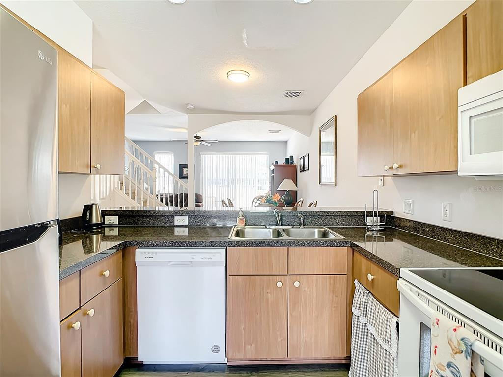 A kitchen with wood cabinets, dark granite countertops, stainless steel appliances, and a pass-through window — 1201 S BEACH CIR, KISSIMMEE, FL