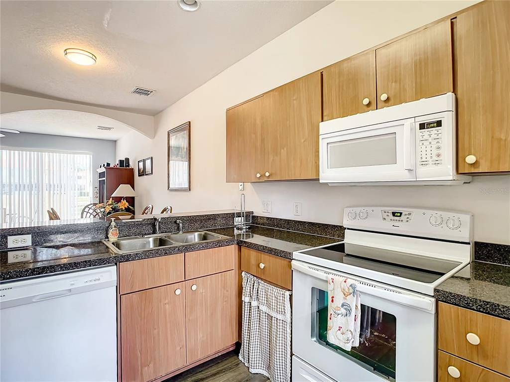 A kitchen features wood cabinets, dark granite countertops, white appliances, and a double-basin sink — 1201 S BEACH CIR, KISSIMMEE, FL