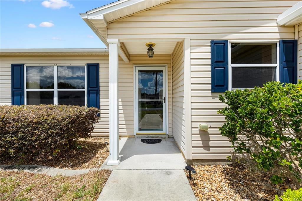 The exterior of a house features beige siding, blue shutters, and a concrete entryway — 3443 SIPSEY STREET, THE VILLAGES, FL